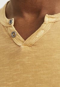 Camisa henley de manga corta en amarillo claro con dos botones de metal en el escote, fabricada con un tejido texturizado y un corte casual.