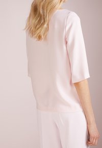 Ljusrosa blus med trekvartsärmar, mjukt tyg, rund halsringning och lös passform, matchad med ljusa byxor.