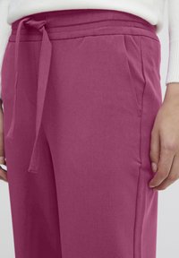 Pink jogger pants with a drawstring waist, side pockets, and smooth texture. Fabric appears soft and casual, suitable for relaxed wear.