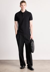 Melna polo krekls ar īsām piedurknēm, ar apkakli un logotipu. Kopā ar vaļīgām melnām biksēm un melnu somu, pabeigts ar melnām kurpēm.