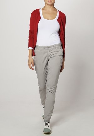 Cardigan rouge, débardeur blanc, chinos gris et baskets multicolores. Matériaux lisses, design ajusté, avec des boutons sur le cardigan.