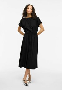 Black maxi dress with short sleeves, gathered elastic waist, and a smooth texture. Paired with silver slingback shoes featuring pointed toes.