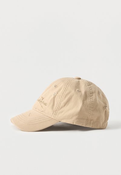 Μπεζ βαμβακερό καπέλο μπέιζμπολ με ελαφρώς φθαρμένες λεπτομέρειες και διακριτικό κεντημένο λογότυπο μπροστά, τοποθετημένο πάνω σε μια απλή λευκή επιφάνεια.