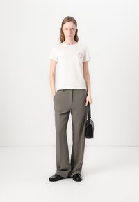 Kortærmet beige bomulds T-shirt med rød cirkulær grafik, parret med løse grå bukser og sorte accessoires, herunder en lille håndtaske.