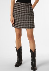 Mini-jupe à motif pied-de-poule en noir et beige, avec une taille cintrée et des poches latérales, associée à des bottes de cowboy noires.