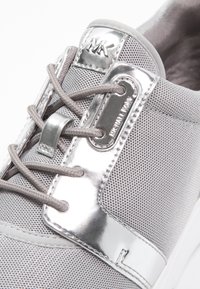 Szare tekstylne sneakersy z metalicznymi srebrnymi akcentami, okrągłymi sznurowadłami i oznaczeniem marki. Teksturowana siateczka i wyściółka z amortyzacją.