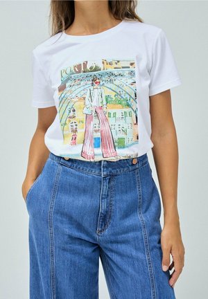 Mujer vistiendo una camiseta blanca con una ilustración colorida de una persona con pantalones a rayas bajo un puente arqueado, combinada con jeans azules de talle alto.