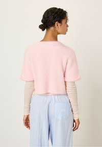 Lichtroze cropped sweater met korte mouwen, zachte textuur, gedragen over een beige langemouwen top, gecombineerd met lichtblauwe gestreepte broek.