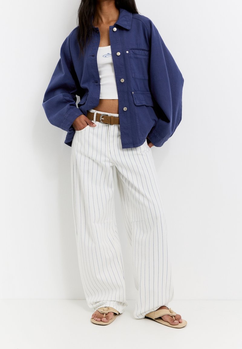 Navy blue oversized jacket with a button front, chest pocket, white striped wide-leg pants, and beige slide sandals.