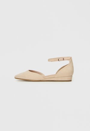 Beige suede flat shoe with a pointed toe, ankle strap with buckle, and low wedge heel. Features a cutout design on the sides.