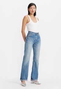 Jeans de denim de tiro alto, de color azul claro, con pierna recta y un ligero deshilachado en el dobladillo, combinados con una camiseta ajustada blanca y zapatos plateados.