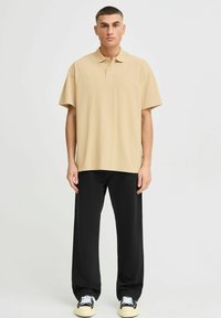 Beige polo-skjorte med klassisk krage, korte ermer og avslappet passform, kombinert med svarte vidde bukser og sneakers.