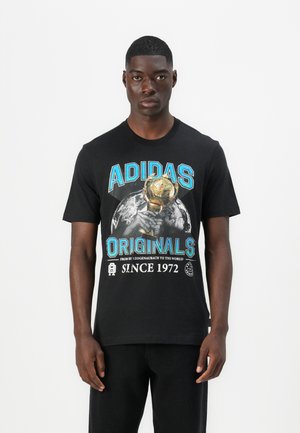 Svart bomull T-skjorte med grafisk trykk av et trofé og Jorden, med teksten 'ADIDAS ORIGINALS' og 'SINCE 1972' i blått og hvitt.