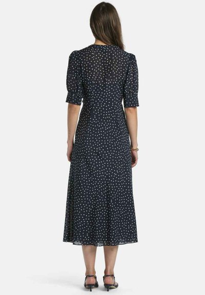 Marineblaues Kleid mit weißen Punkten, kurzen Puffärmeln und einem fließenden midilangen Rock. Die Rückseite hat einen einfachen Ausschnitt und einen kleinen Schlitz.
