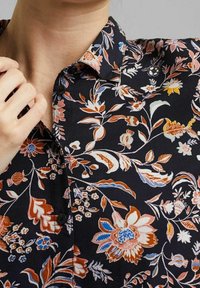 Långärmad blommig blus i svart med en mängd färgglada blommönster, klassisk krage och knapplist fram. Slät tygtextur.