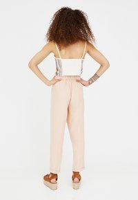 Twee-delige outfit met een fitted, meerkleurig gestreept crop top en losse, lichtroze broeken. Het model draagt bruine plateau sandalen.