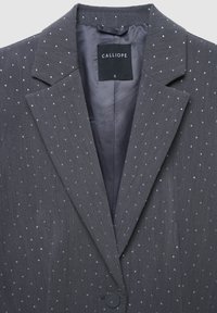 Blazer grigio scuro con piccole stelle riflettenti, revers a punta, chiusura a un bottone e etichetta nera all'interno del colletto con la scritta "Calliope S."
