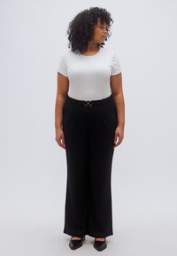 Λευκό τοπ με κοντά μανίκια συνδυασμένο με ψηλόμεσο, φαρδύ μαύρο παντελόνι με ασημένια αγκράφα ζώνης, παρουσιασμένο σε ουδέτερο φόντο.