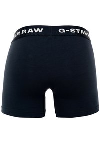 Boxers oscuros de color azul con un diseño ajustado, que presentan una cinturilla ancha etiquetada "G-STAR RAW" en blanco. Textura suave y sin patrones visibles.