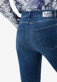 Vaqueros de mezclilla en un lavado azul oscuro con una silueta ajustada, que cuentan con dos bolsillos traseros y un parche de cuero con la marca en la cinturilla.