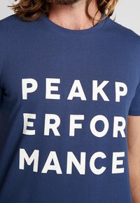 Námořnická modrá bavlněná tričko s tučným bílým textem "PEAK PERFORMANCE", krátké rukávy a kulatý výstřih.