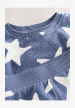 Felpa in pile blu con motivi a stelle bianche, scollo arrotondato e polsini a coste. Texture morbida con un design accogliente.