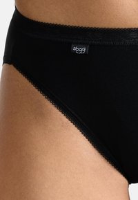 Schwarzer Baumwollslip mit glatter Textur, verziert mit einer gewellten Spitzenborte und einem kleinen Logotag am Bund.