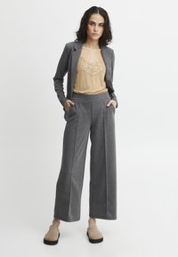 Sivina blazer s prilagojenim krojem, v kombinaciji s širokimi sivimi hlačami. Pod njim bež čipkast top. Teksturobna tkanina po celotni površini.