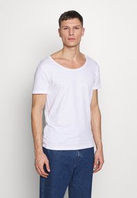 Weißes T-Shirt mit kurzen Ärmeln und U-Boot-Ausschnitt, aus weichem, leichtem Material; kombiniert mit blauen Jeans.