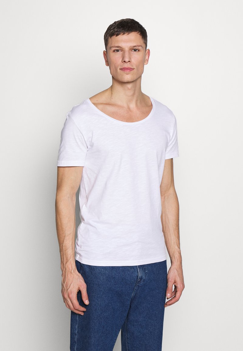 Weißes T-Shirt mit kurzen Ärmeln und U-Boot-Ausschnitt, aus weichem, leichtem Material; kombiniert mit blauen Jeans.