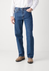 Jean en denim bleu avec une coupe droite, poches avant et fermeture à bouton. Le tissu a une texture en denim classique.