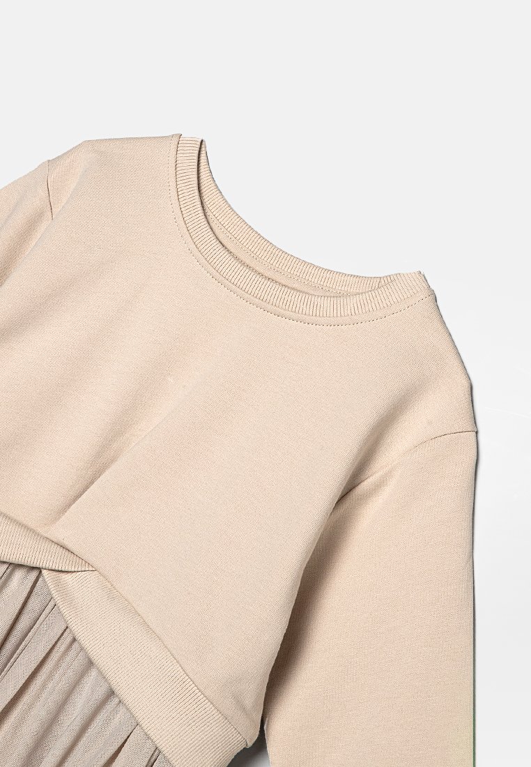 Beige långärmad stickad tröja med ribbad rundhals och nederkant, tillsammans med en matchande veckad kjol, lagd platt på en vit bakgrund.