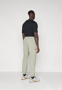 Pantalones cargo de color verde claro con puños elásticos, bolsillos laterales y una cintura con cordón, combinados con una camiseta negra de manga corta y zapatillas.