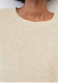 Pull en maille beige clair avec une finition texturée, présentant un col rond côtelé. Le tissu semble doux et confortable.