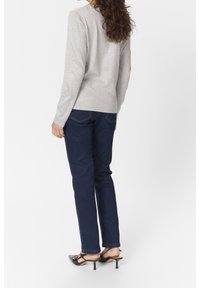 Graues Langarmoberteil und dunkelblaue gerade Jeans mit klassischer Passform. Schwarze spitze Absatzschuhe mit Hardware-Details.