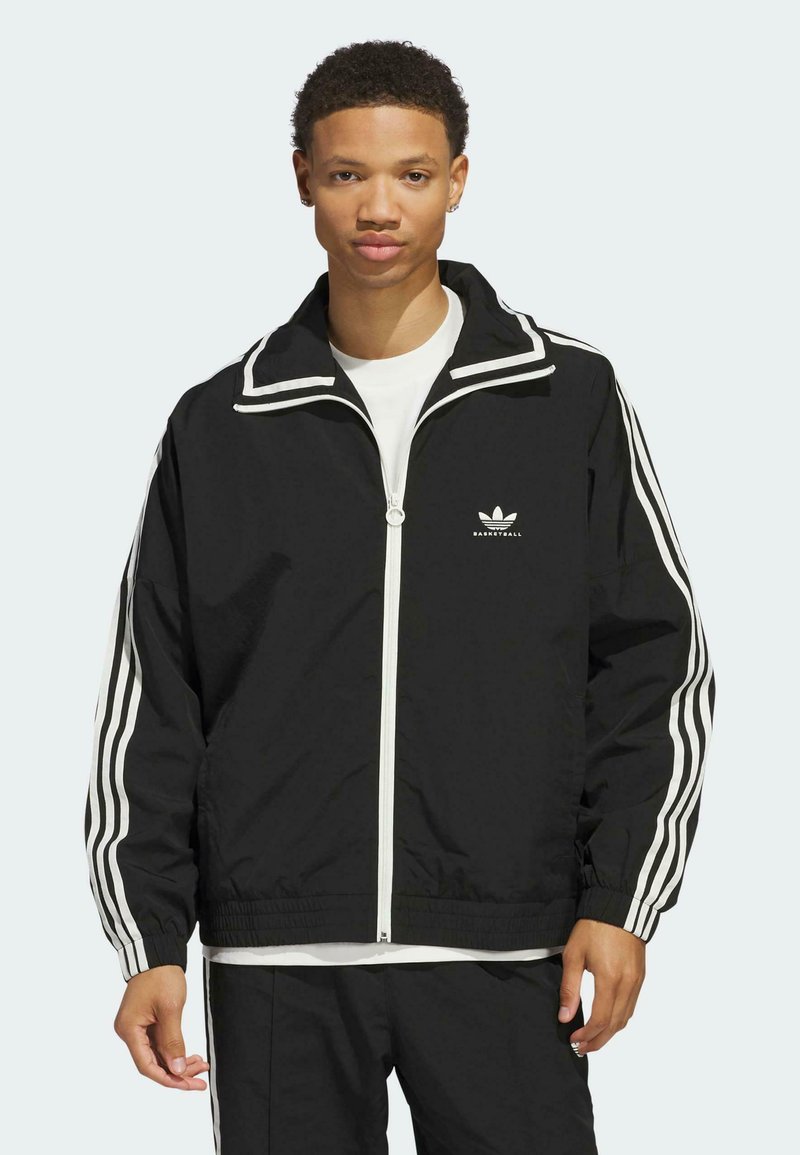 Schwarze Zip-Jacke mit weißen Streifen an den Ärmeln und am Kragen. Sie hat eine entspannte Passform, elastische Bündchen und ein gesticktes Logo auf der Brust.