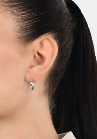 Pendientes de aro de plata exhibidos en la oreja de un modelo, con un acabado suave y pulido y un diseño ligeramente retorcido para añadir textura.