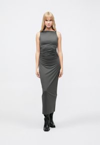 Bezroku, tumši pelēka, ķermeņa veidā pieguļoša maxi kleita ar savilktu detaļu pie vidukļa, kombinēta ar melnām potīšu zābakām. Gluda, elastīga auduma.