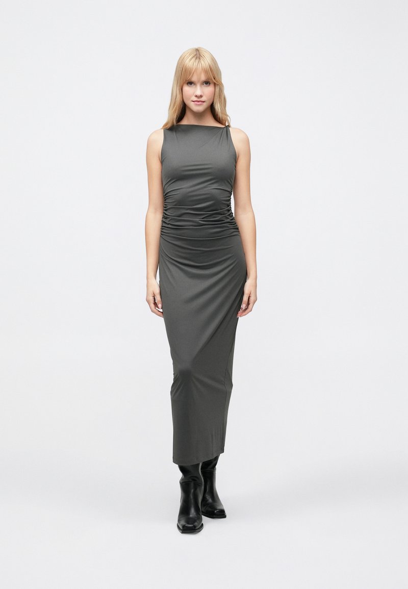 Bezroku, tumši pelēka, ķermeņa veidā pieguļoša maxi kleita ar savilktu detaļu pie vidukļa, kombinēta ar melnām potīšu zābakām. Gluda, elastīga auduma.