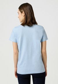 Jasnoniebieski t-shirt z krótkim rękawem uszyty z miękkiego, gładkiego materiału. Posiada okrągły dekolt oraz luźny krój, wykończony w talii i przy rękawach.