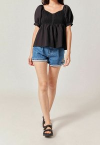 Black, smocked blouse with short puff sleeves paired with denim shorts featuring a rolled hem and embroidered detail. Black sandals complete the look.