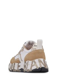 Sneaker features white textile with beige suede accents, a chunky white and black sole, and bold lettering along the bottom.