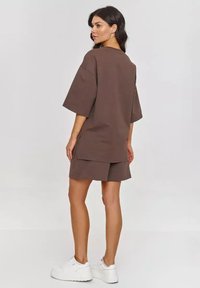 Brązowa, oversize t-shirt i dopasowane szorty wykonane z teksturowanej tkaniny; noszone z białymi sneakersami; widoczny boczny rozporek na krawędzi koszulki.