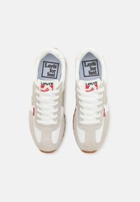 Zapatillas Levi's con parte superior de ante gris, detalles en textil blanco, cordones blancos y suelas de goma marrón. Presenta un gran logo en la lengua.