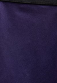 Κοντινή λήψη σκουρόχρωμου μωβ υφάσματος με λεπτή κάθετη ριμπ υφή και μαύρο υφασμάτινο άκρο στο πάνω μέρος.