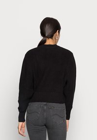 Schwarzer gestrickter Pullover mit gerippter Textur, Rundhalsausschnitt und fallenden Schultern. Verfügt über einen cropped Saum mit gerippten Ärmeldetails.