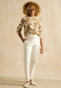 Bluza albă cu mâneci lungi și model floral maro, asortată cu pantaloni crem cu talie înaltă și pantofi albi slip-on. Material neted, croială lejeră.