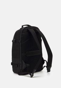 Sac à dos noir au design élégant et texturé, doté de panneaux en maille, de bretelles réglables et de plusieurs accents de boucle pour une fermeture sécurisée.