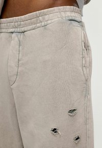 Lichtgrijze sweatpants van zachte stof, met zichtbare versleten details, drie uitsparingen en een gestikte tailleband.