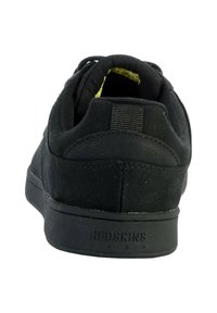 Zapatilla negra con parte superior de lona y suela de goma. Presenta un respaldo texturizado con un logotipo grabado en el talón y un cuello acolchado para mayor comodidad.